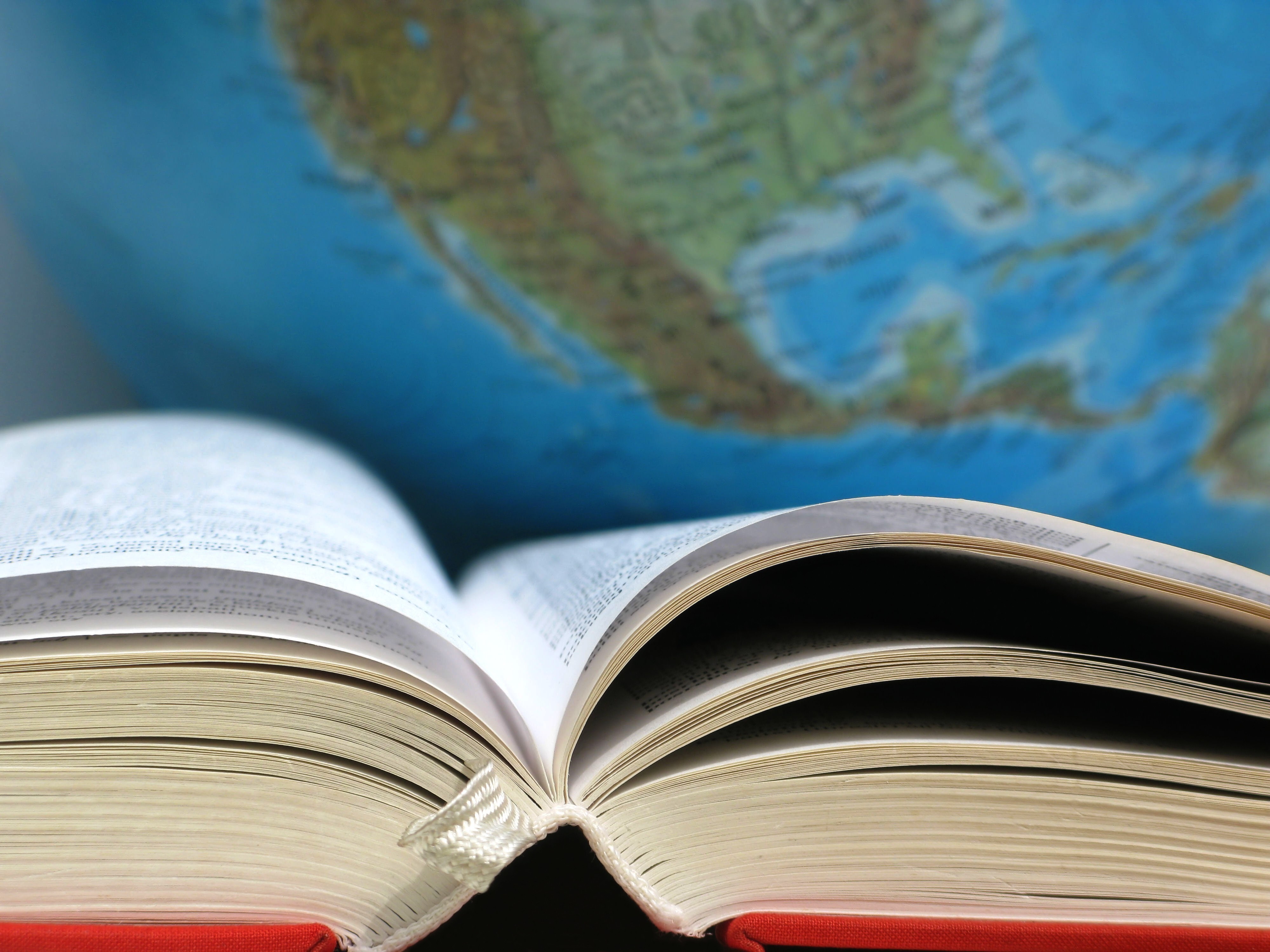 aufgeklapptes Buch mit Weltkugel im Hintergrund